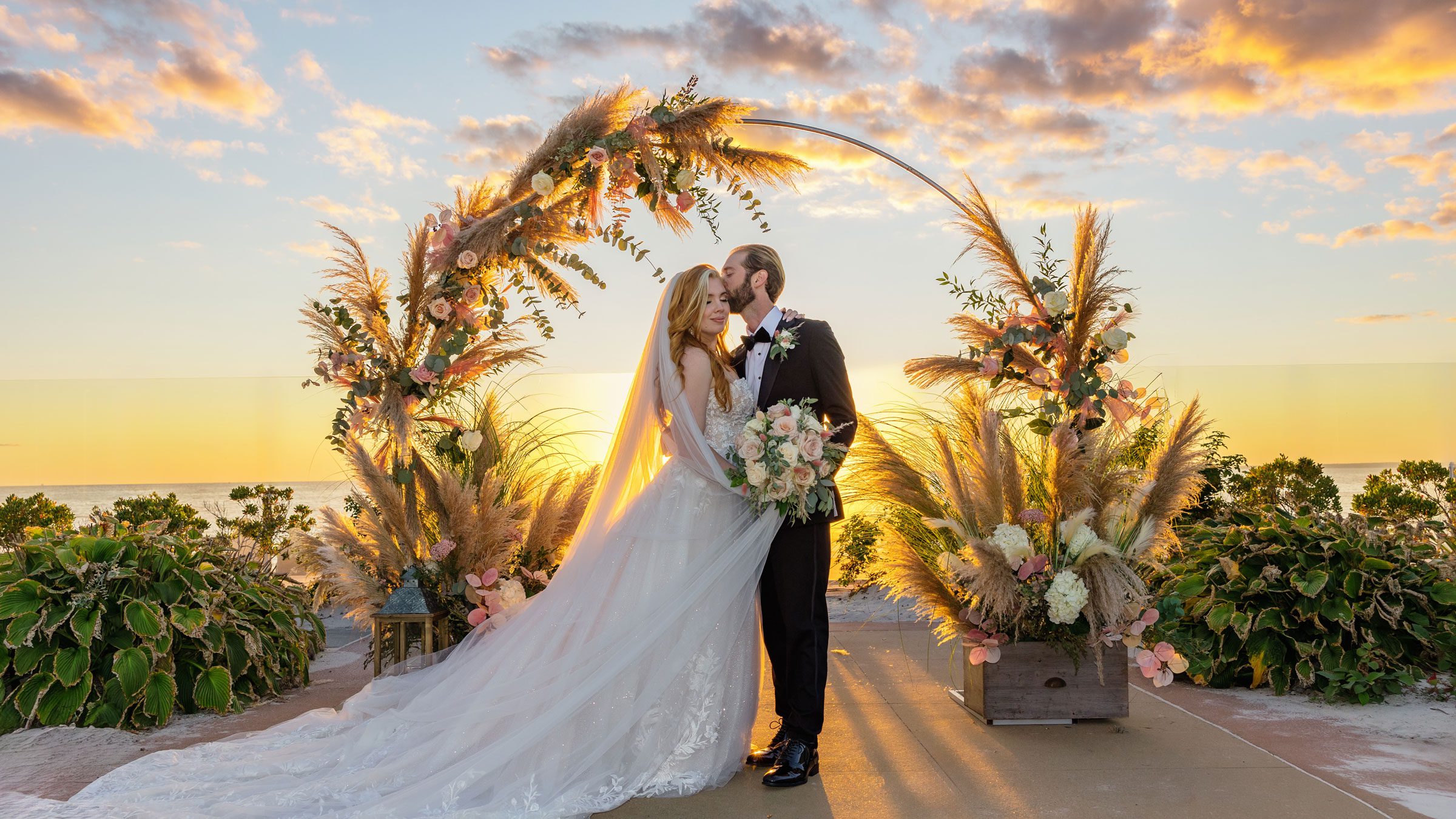 Sunset wedding portrait of bride and groom kissing under a pampas grass floral arch at SeaCrest Beach Hotel, Cape Cod.